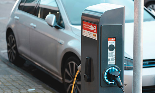 Photo d'une voiture électrique gris métallisé, branchée à une borne de recharge.